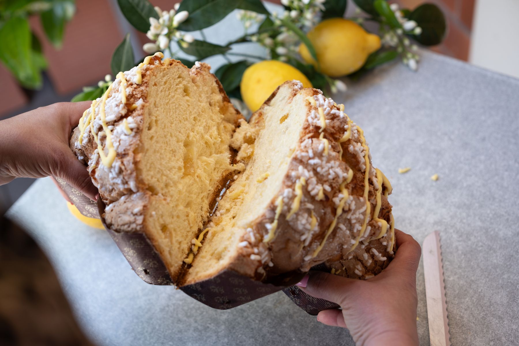 Persona che tiene in mano una torta al limone appena tagliata. La torta è gialla e glassata.