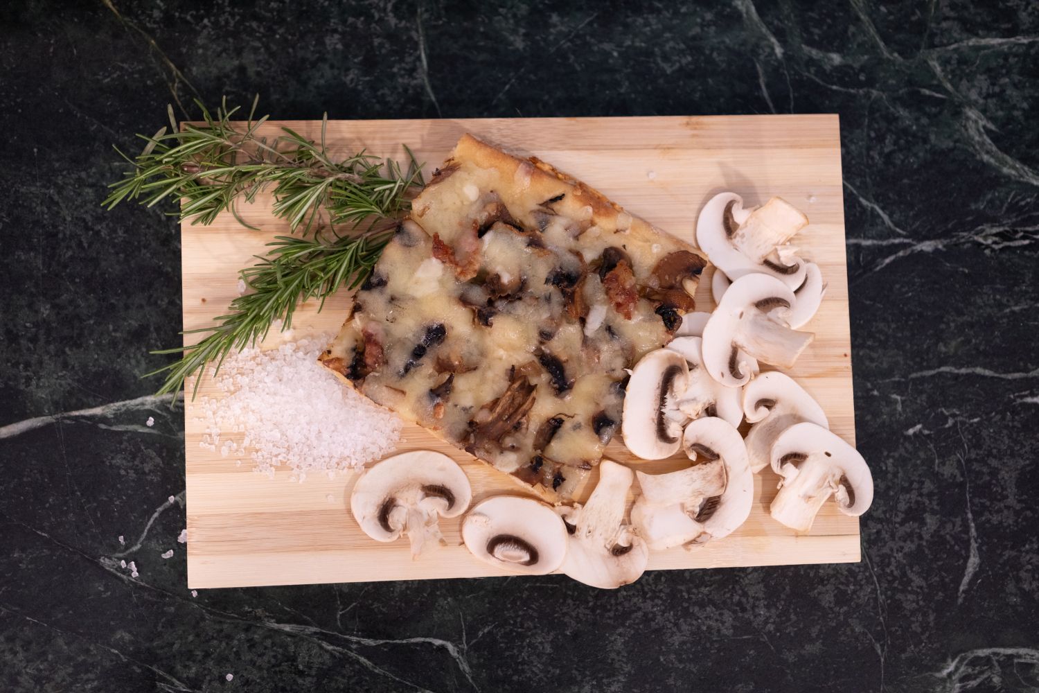 Torta di funghi su un tagliere di legno, guarnita con rosmarino, funghi affettati e sale.