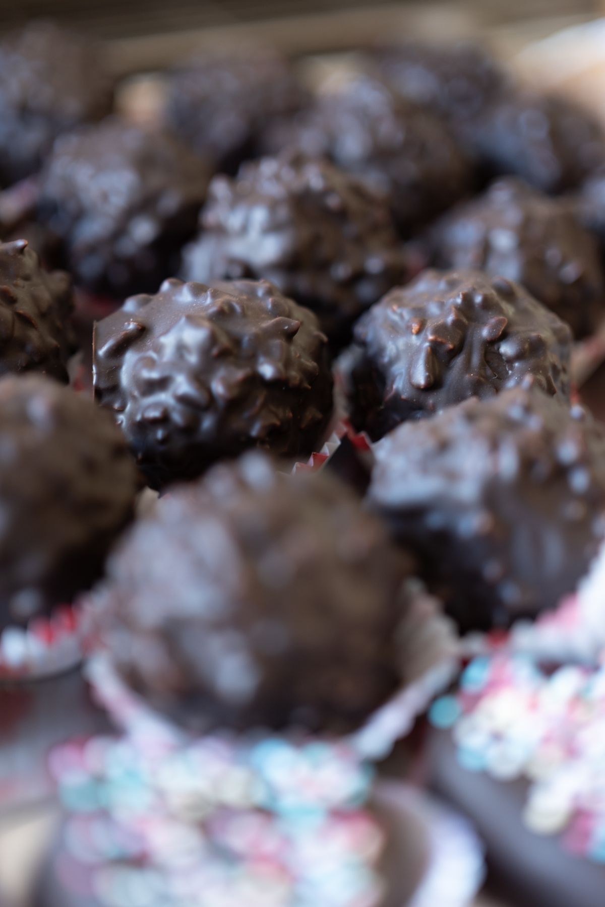 Tartufi al cioccolato, ricoperti di cioccolato fondente, in pirottini di carta con granella colorata.