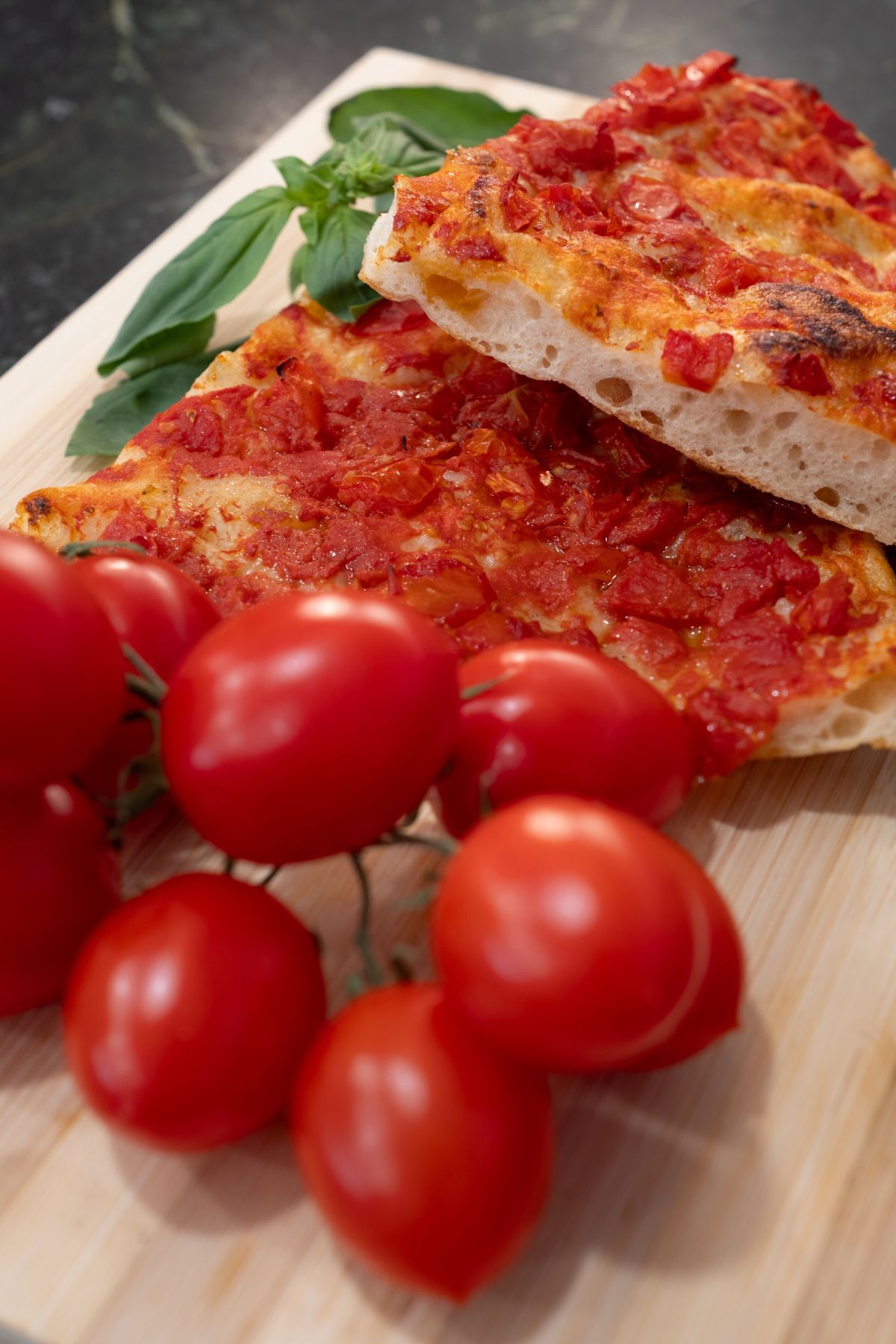 Fette di pizza con salsa di pomodoro, pomodorini e basilico su un tagliere di legno.