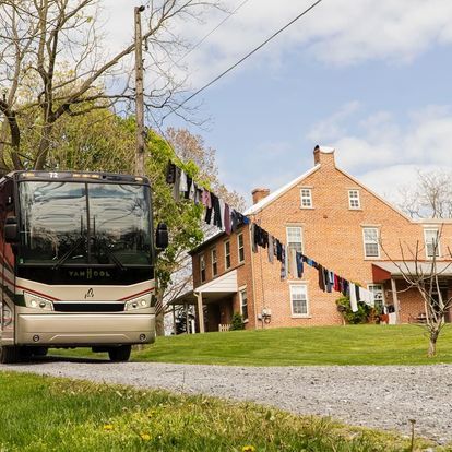 A vanhool bus is parked in front of a brick house