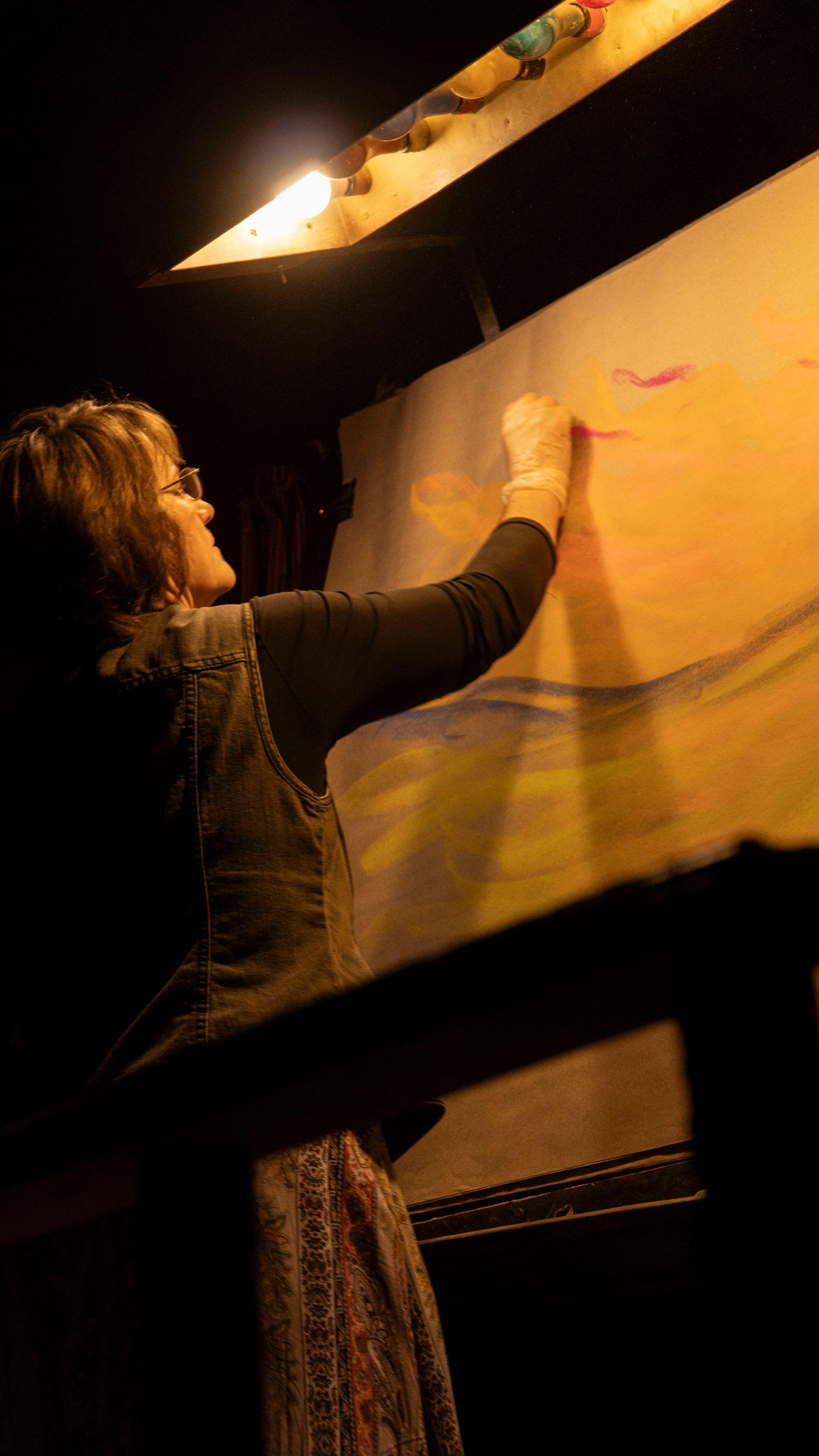 A woman is painting on a large canvas in a dark room.