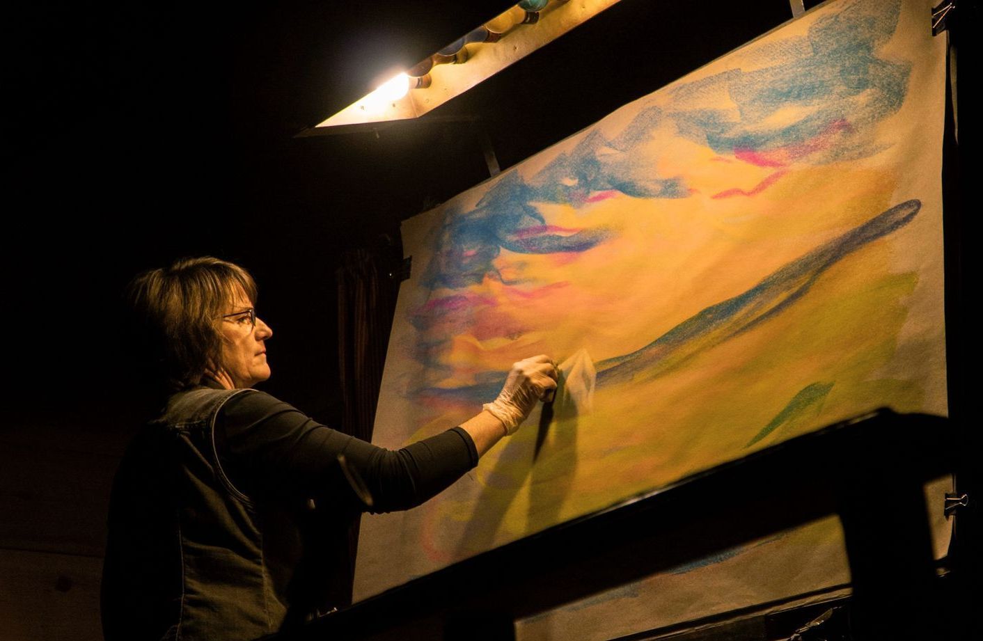 A woman is painting on a large canvas in a dark room