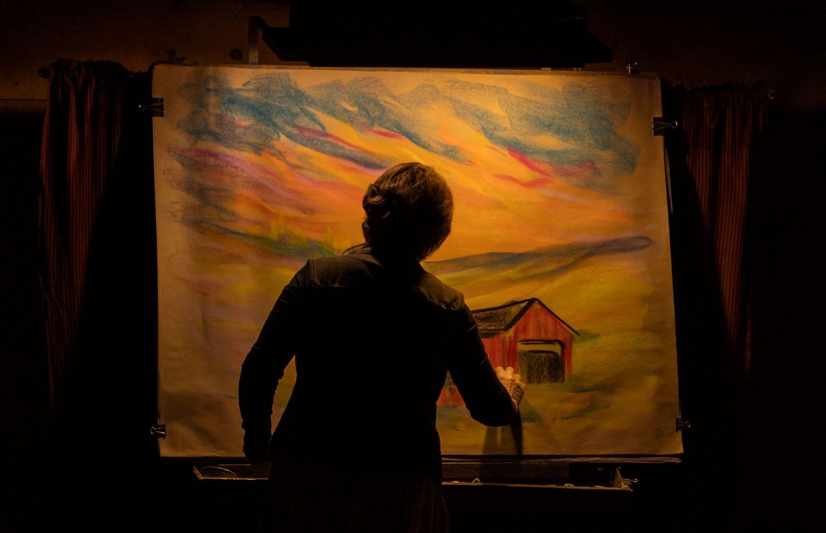 A woman is standing in front of a large painting of a barn.