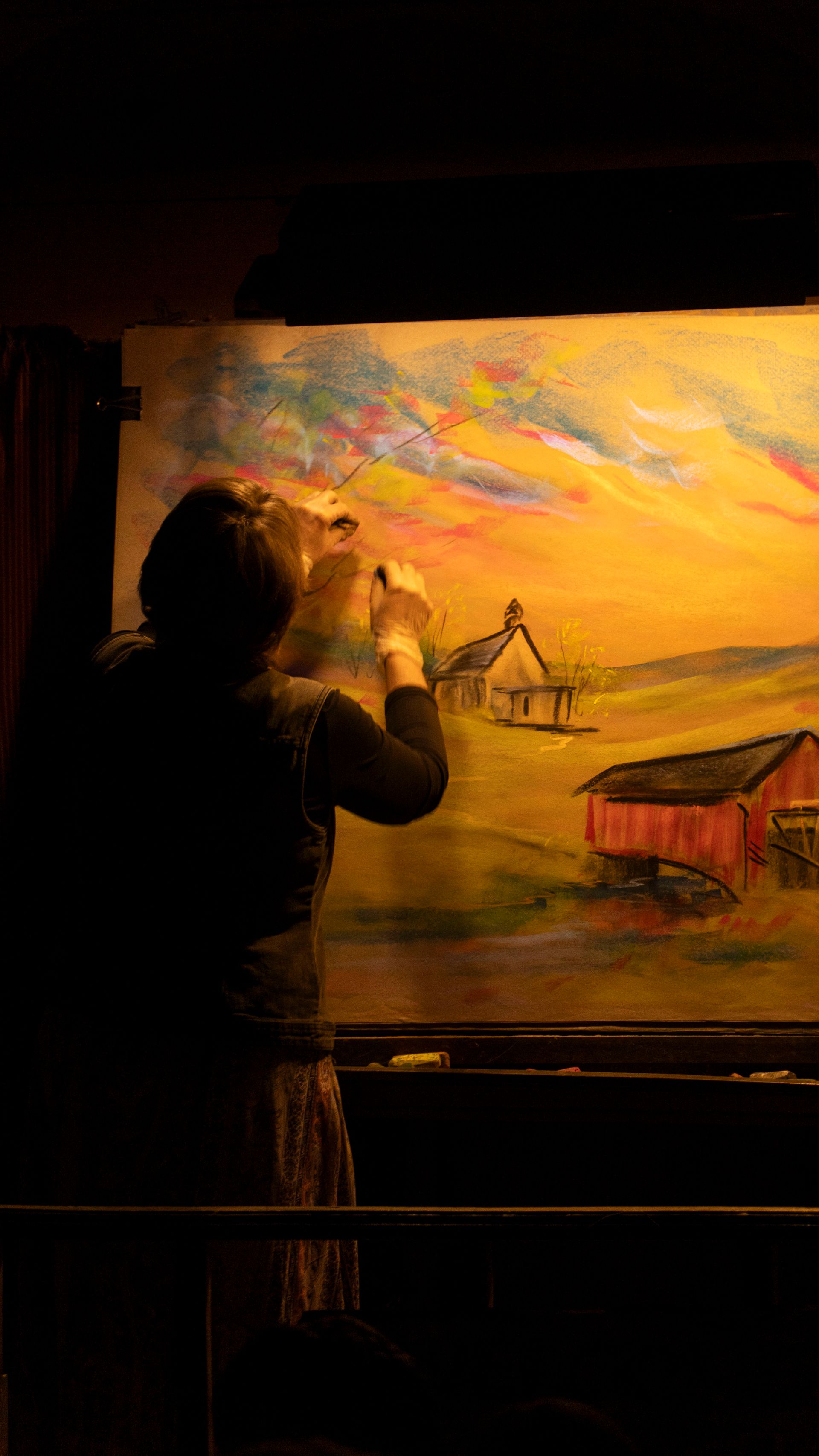 A woman is painting a picture of a barn on a canvas.