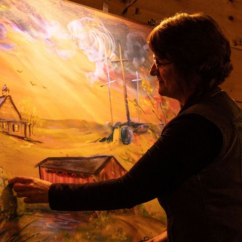 A woman is painting a picture of a church and a barn