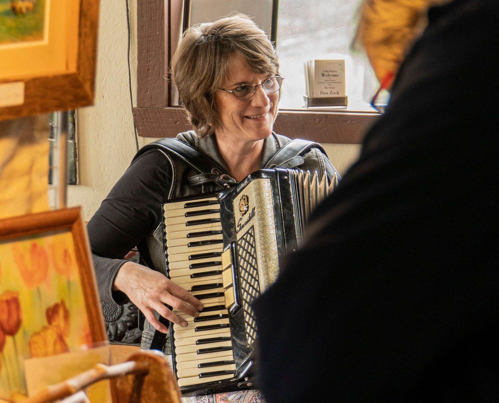 A woman is playing an accordion in front of a window