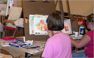 A woman in a pink shirt is painting on an easel