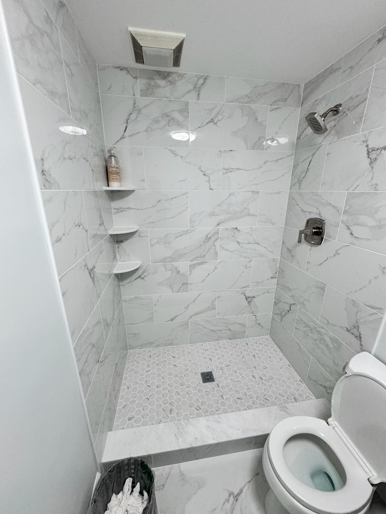 Small white tiled bathroom with a walk-in shower and a toilet in the foreground.
