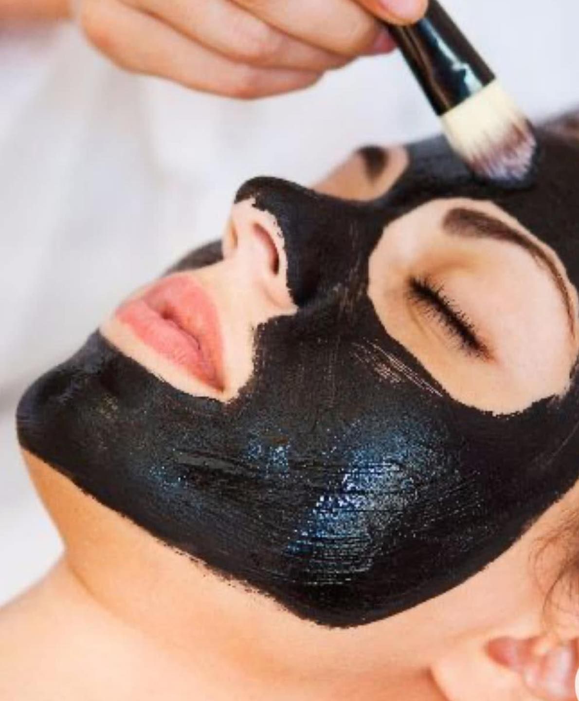 A Woman is Getting a Black Mask Applied to Her Face — Renew Laser Clinic in Taree, NSW