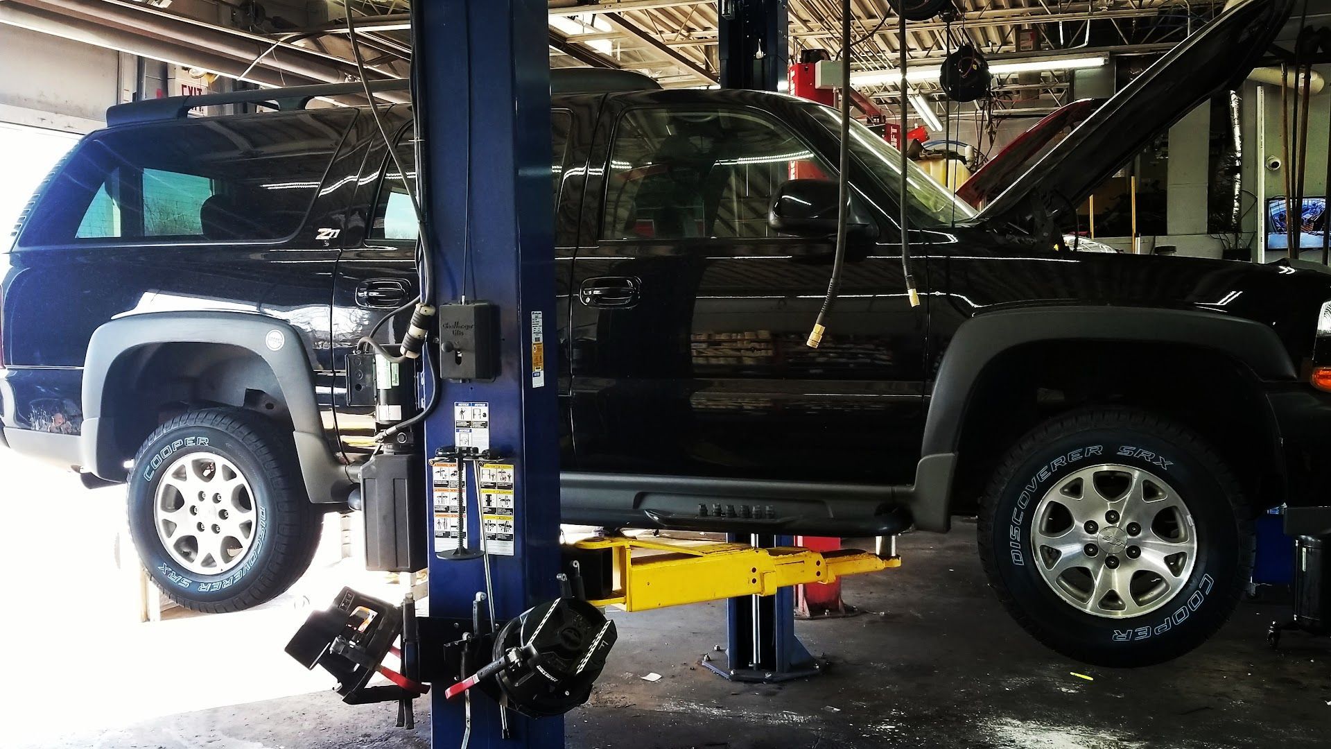 A black SUV is lifted on a mechanical automotive hoist inside a repair garage with its hood open. | Homestead Auto & Tire