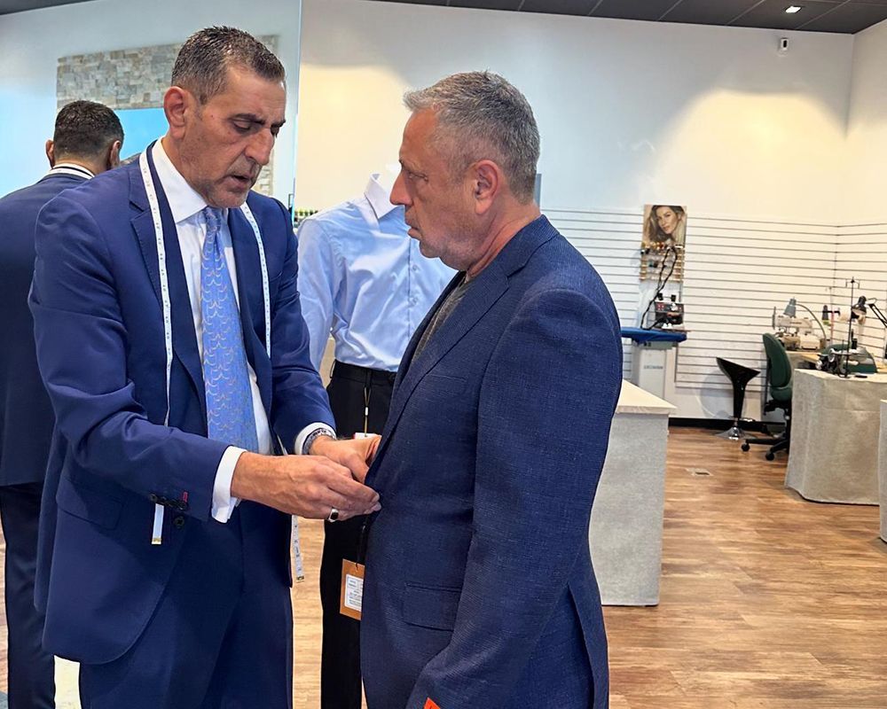 Two men in suits, one measuring the other's suit jacket in a store.