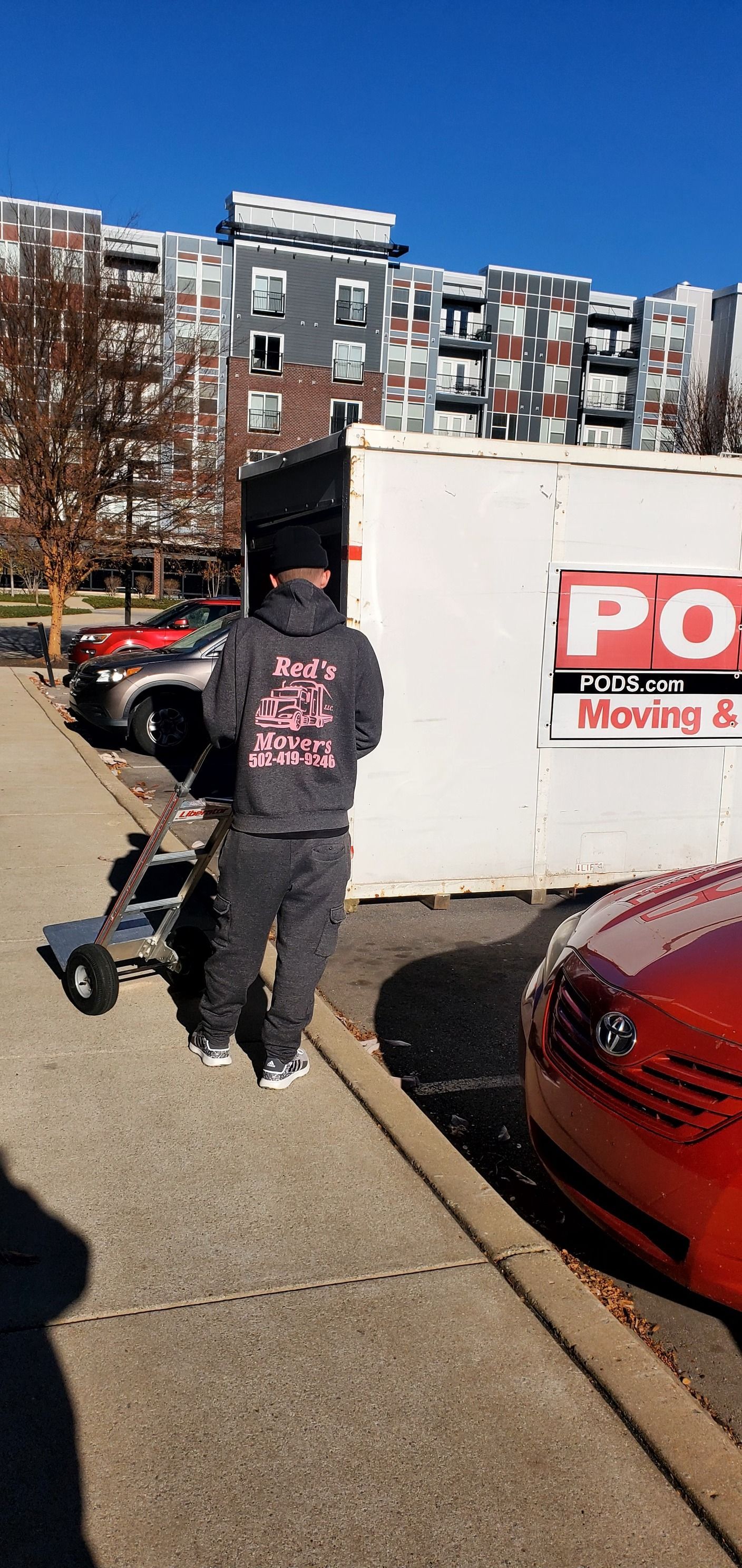 A man is pushing a box down a sidewalk next to a moving truck.