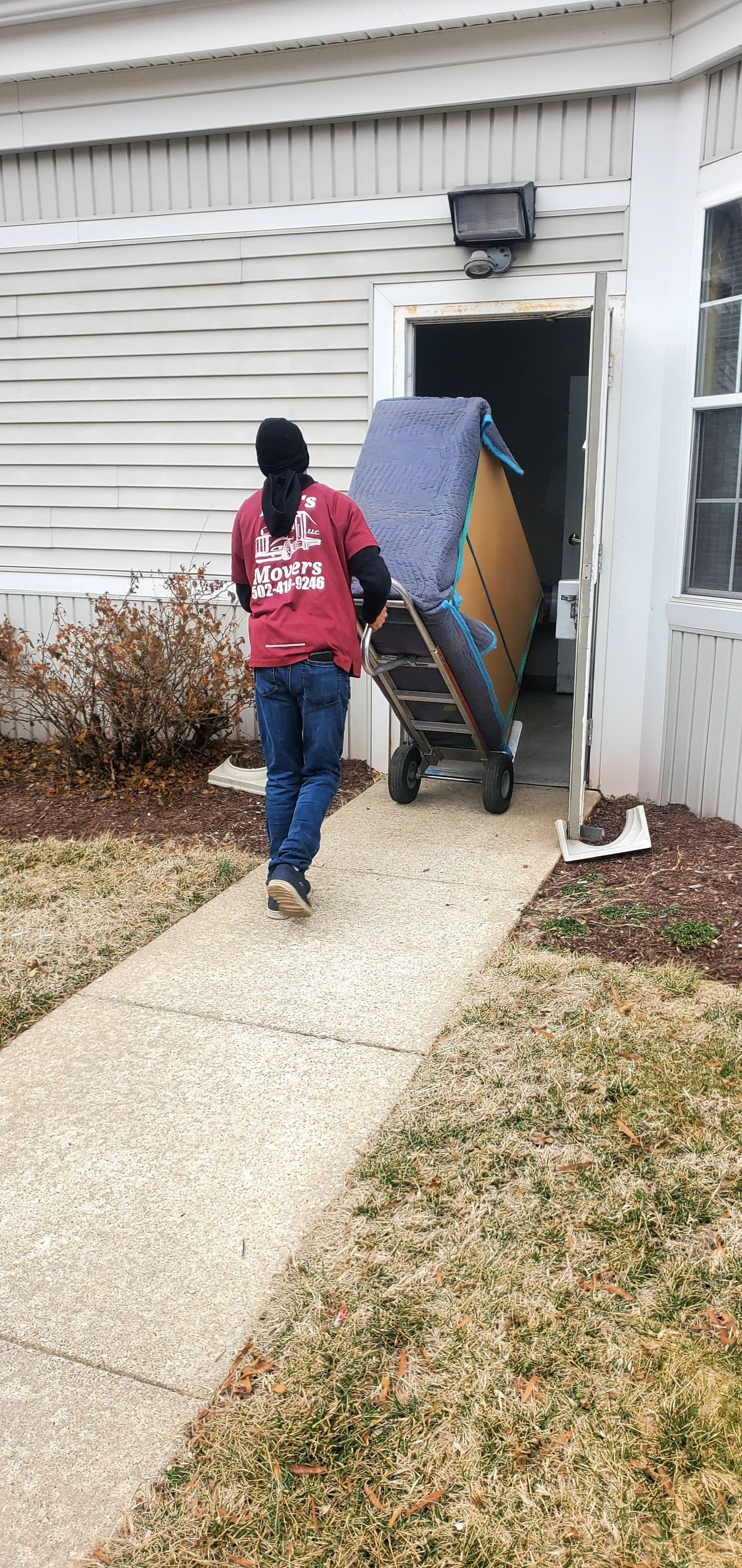 A man is pushing a mattress on a dolly into a house.