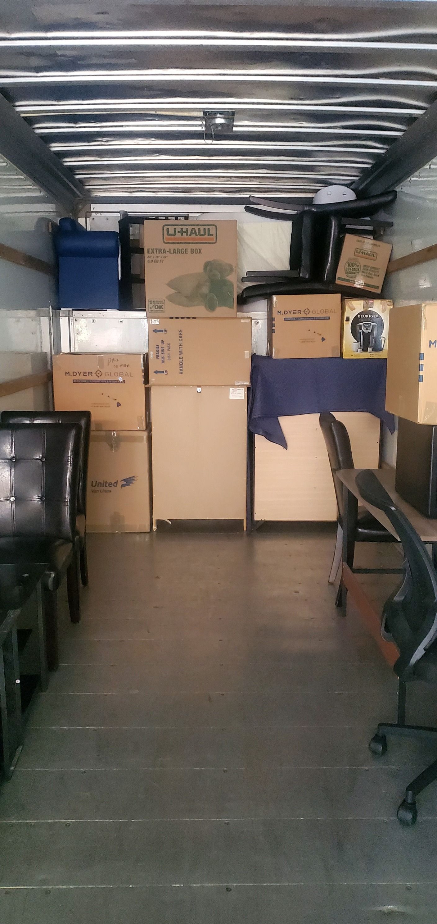 The inside of a moving truck filled with boxes and chairs.