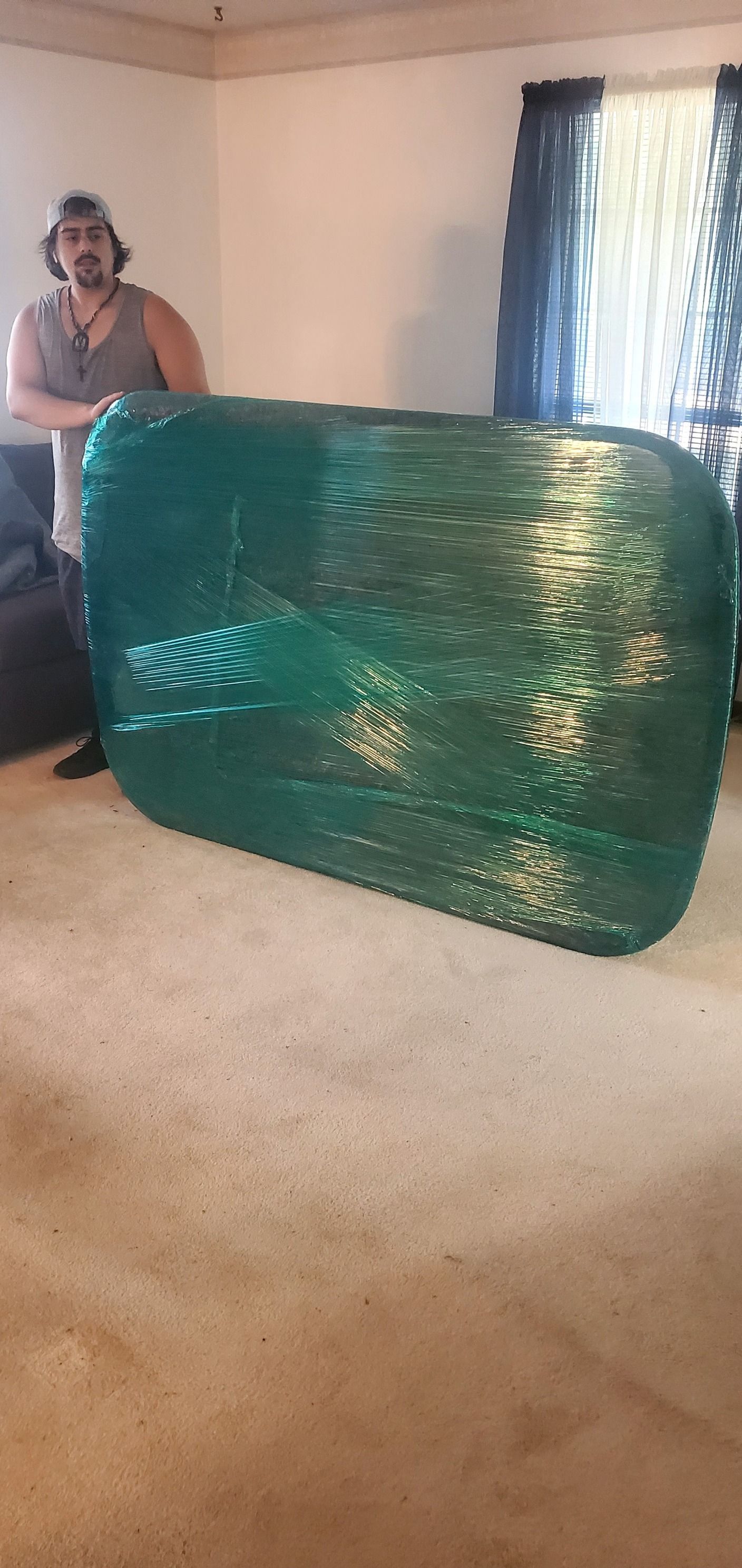 A man is standing next to a couch wrapped in green plastic wrap.