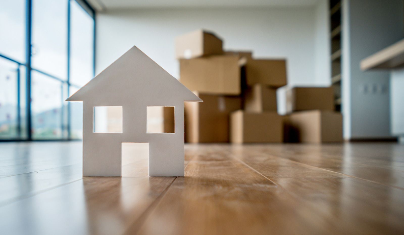 A model house is sitting on a wooden floor next to a pile of cardboard boxes.