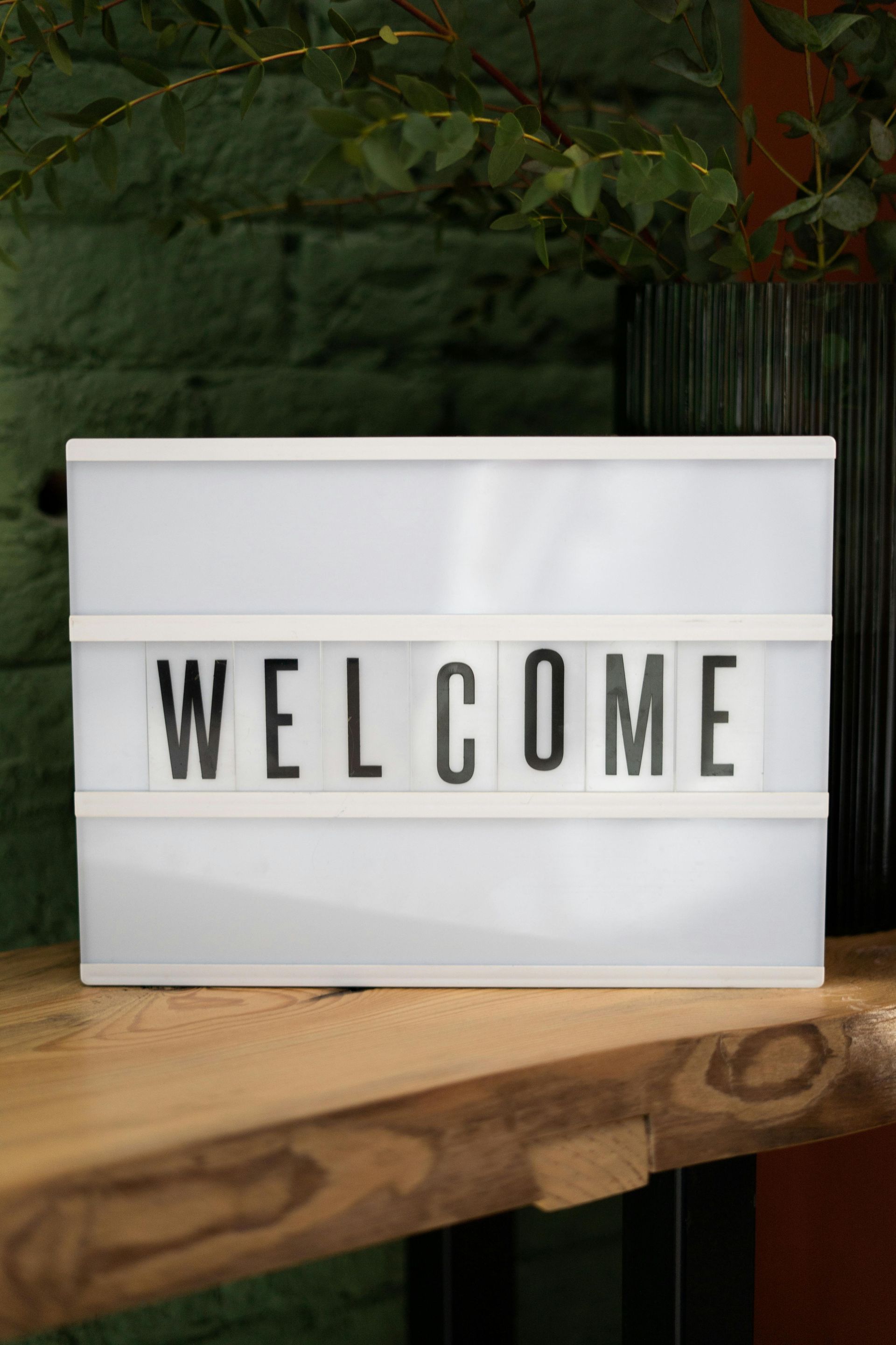 A white sign that says welcome is sitting on a wooden table.