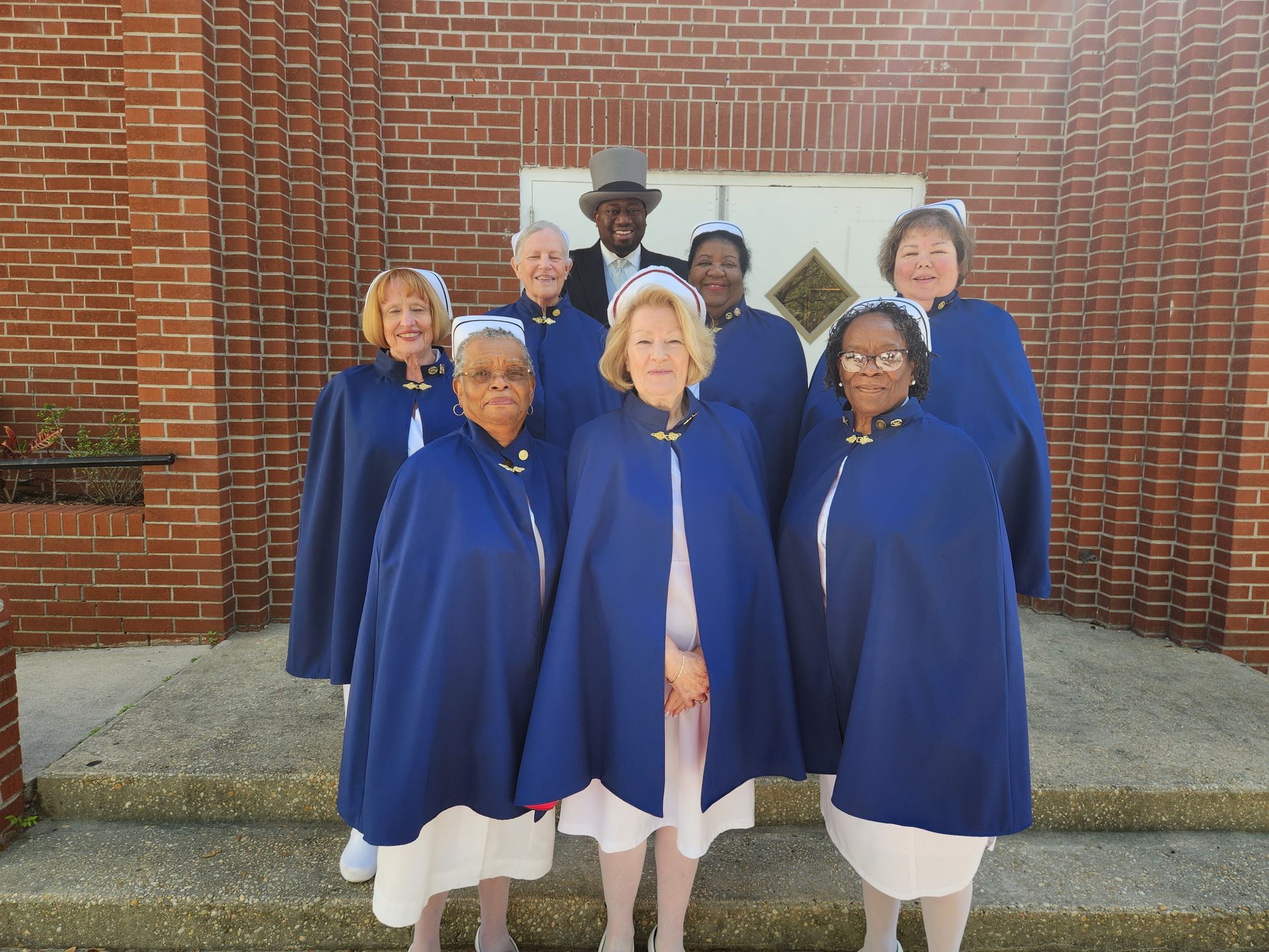 A group of nurses are posing for a picture in front of a brick building.