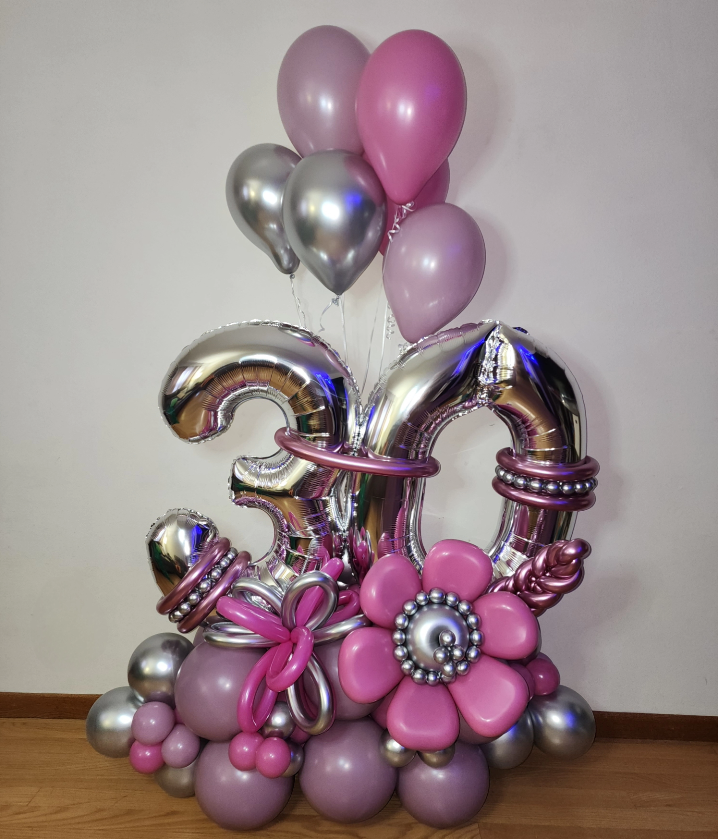A bunch of pink and silver balloons are sitting on a wooden floor.
