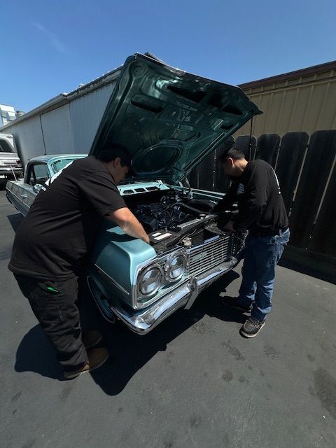Two men are working on a car with the hood open