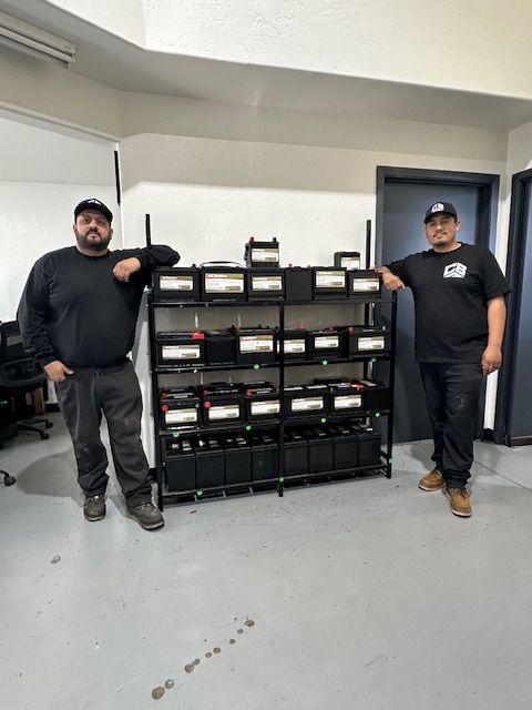 Two men are standing in front of a shelf full of batteries.