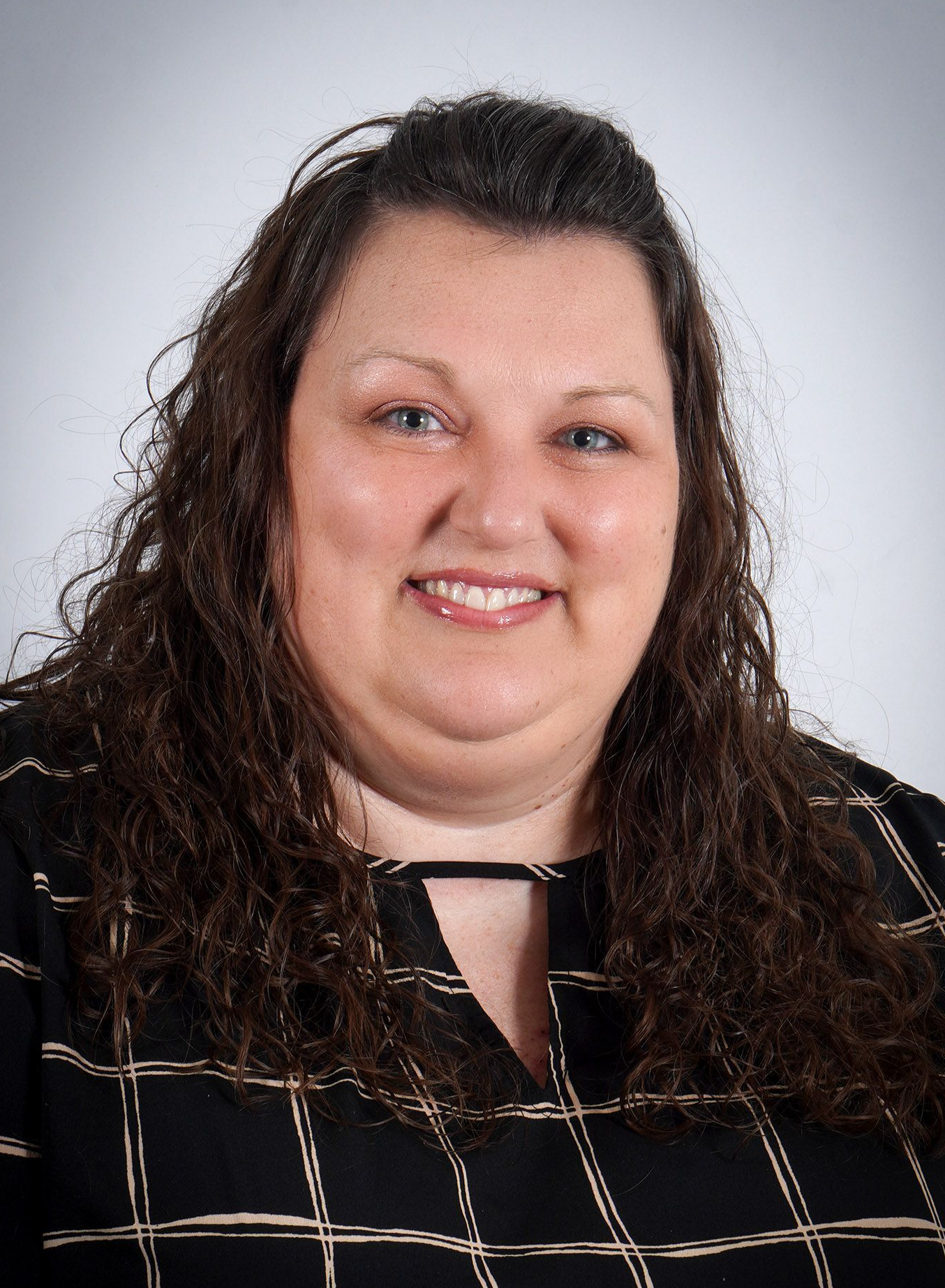 A woman with curly hair and blue eyes is smiling for the camera.