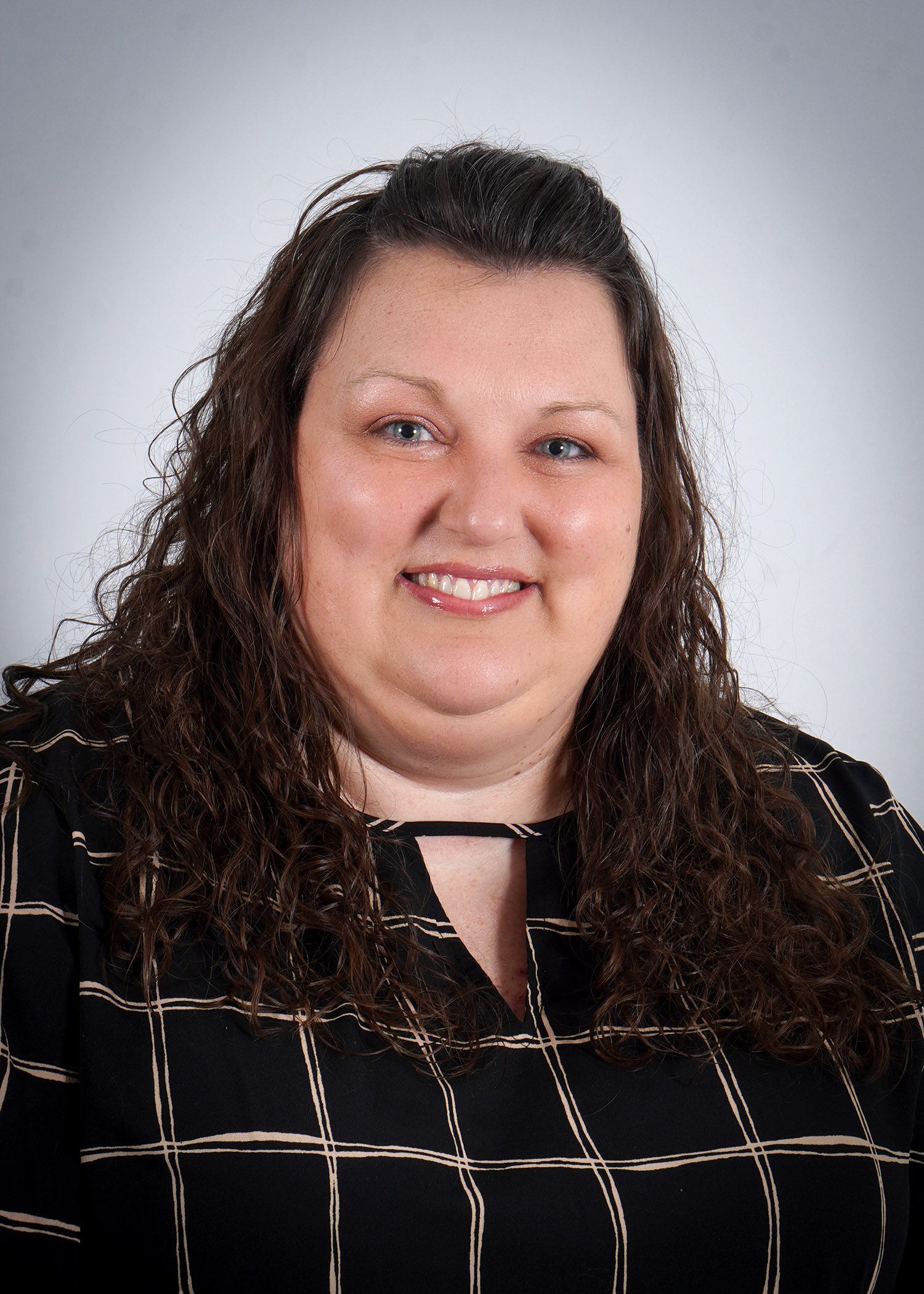 A woman with curly hair and blue eyes is smiling for the camera.