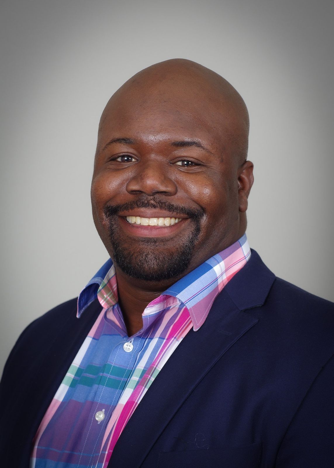 A man in a suit and plaid shirt is smiling for the camera.