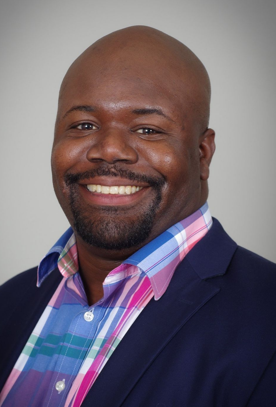 A man in a suit and plaid shirt is smiling for the camera.