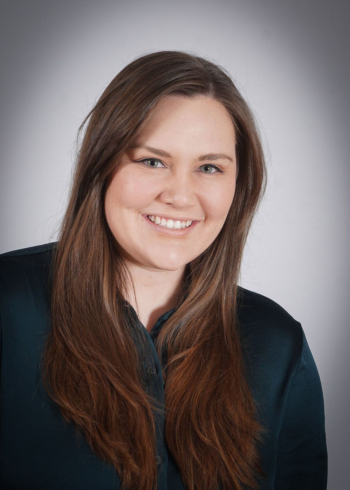 A woman with long brown hair is smiling and wearing a blue shirt.