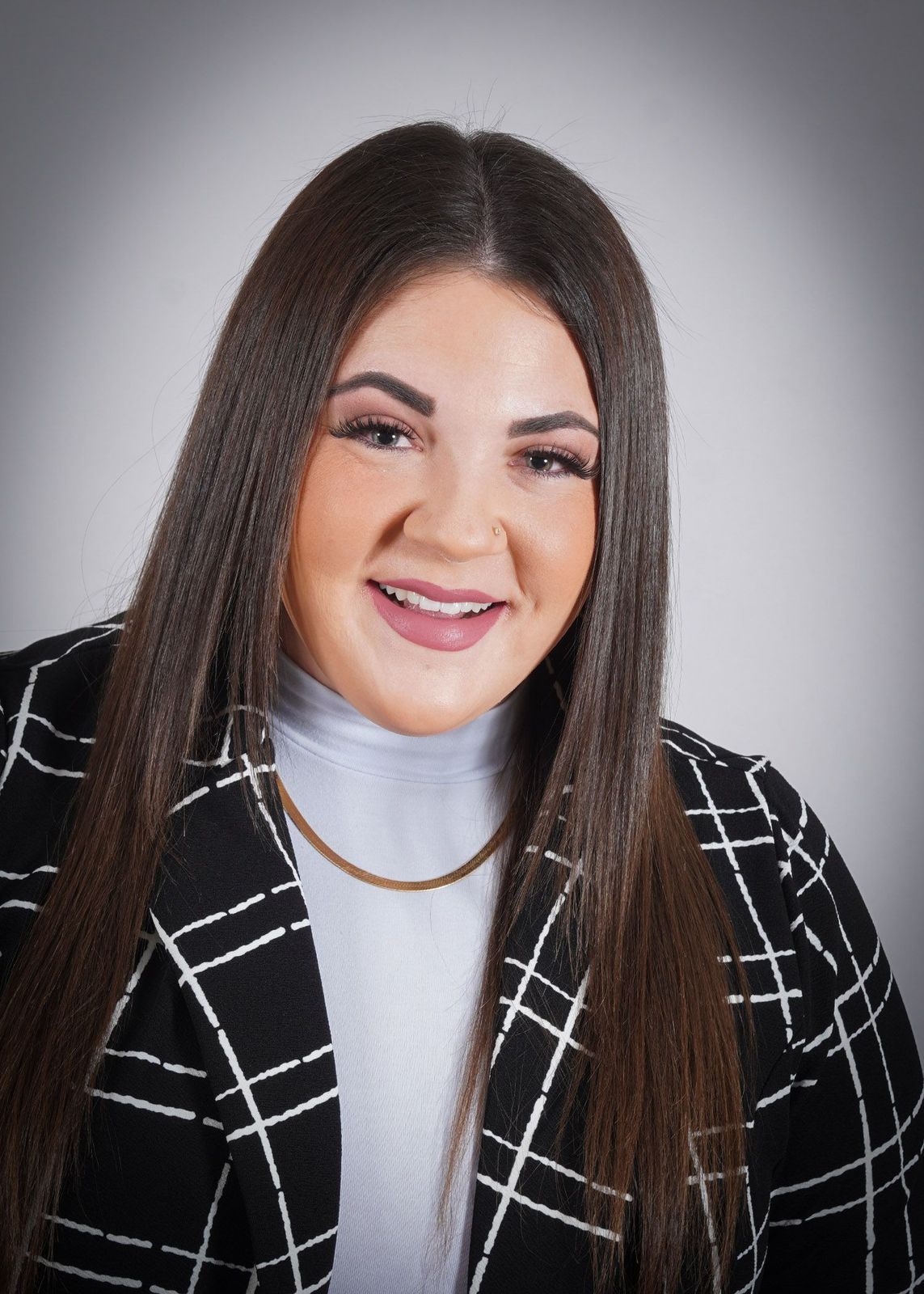 A woman with long hair is wearing a black and white plaid jacket and a white turtleneck.