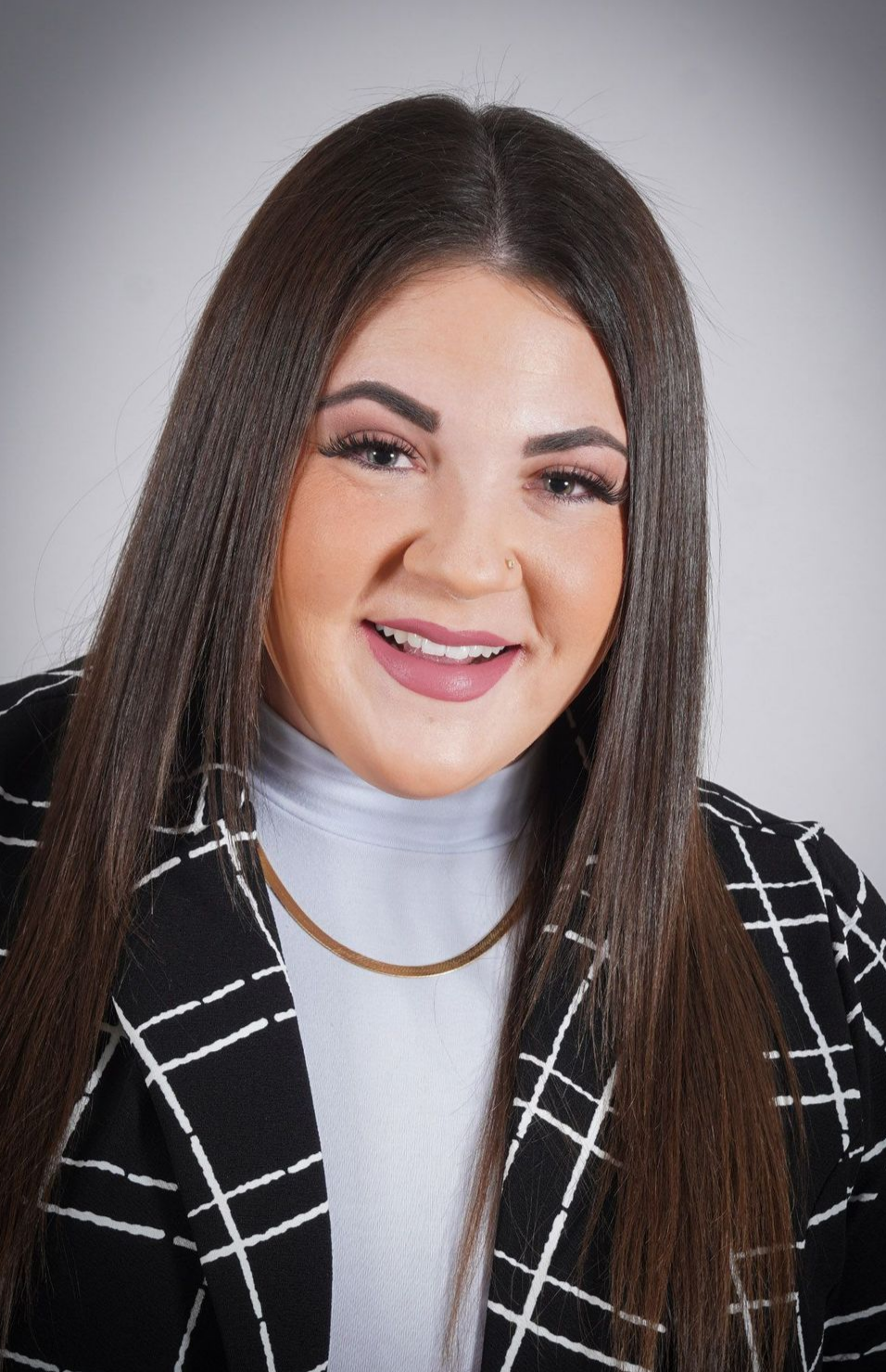 A woman with long hair is wearing a black and white plaid jacket and a white turtleneck.