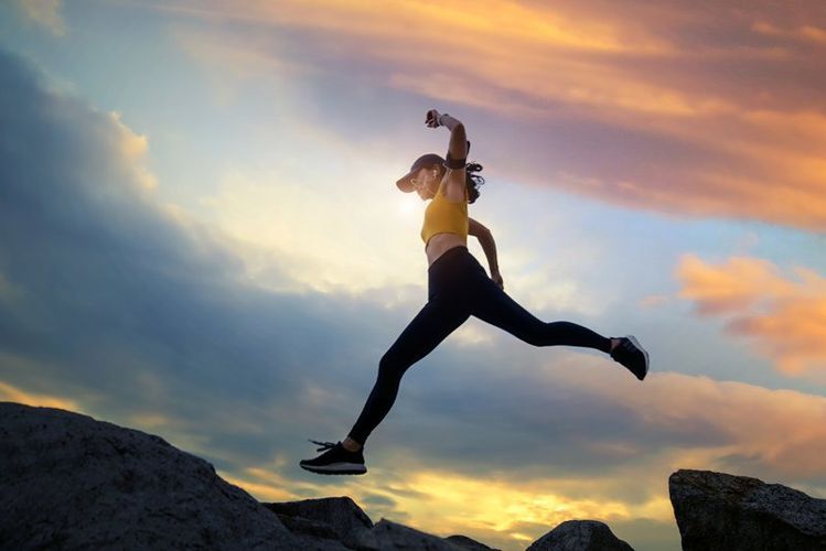 A woman is jumping over a rock at sunset.