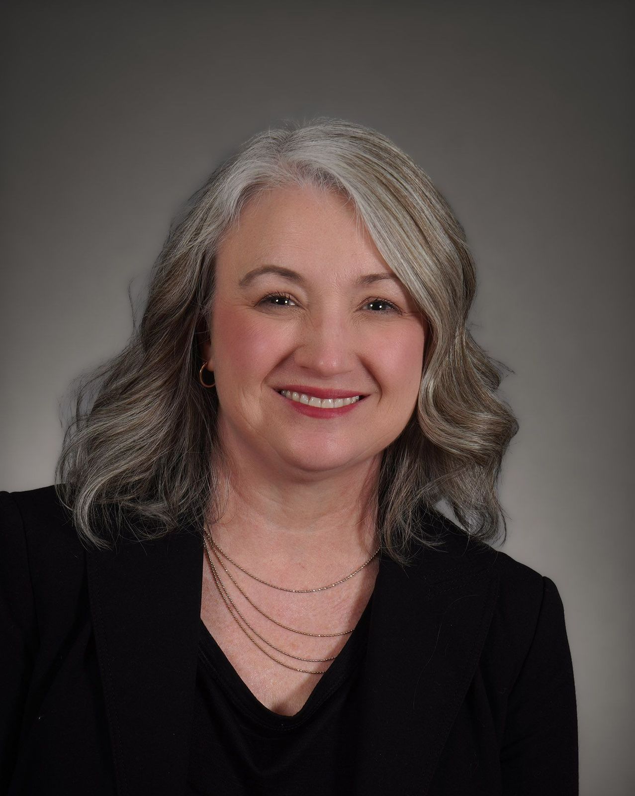 A woman with gray hair and a black shirt is smiling for the camera.