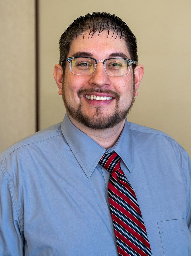 Man wearing glasses, blue shirt, red striped tie, smiling.