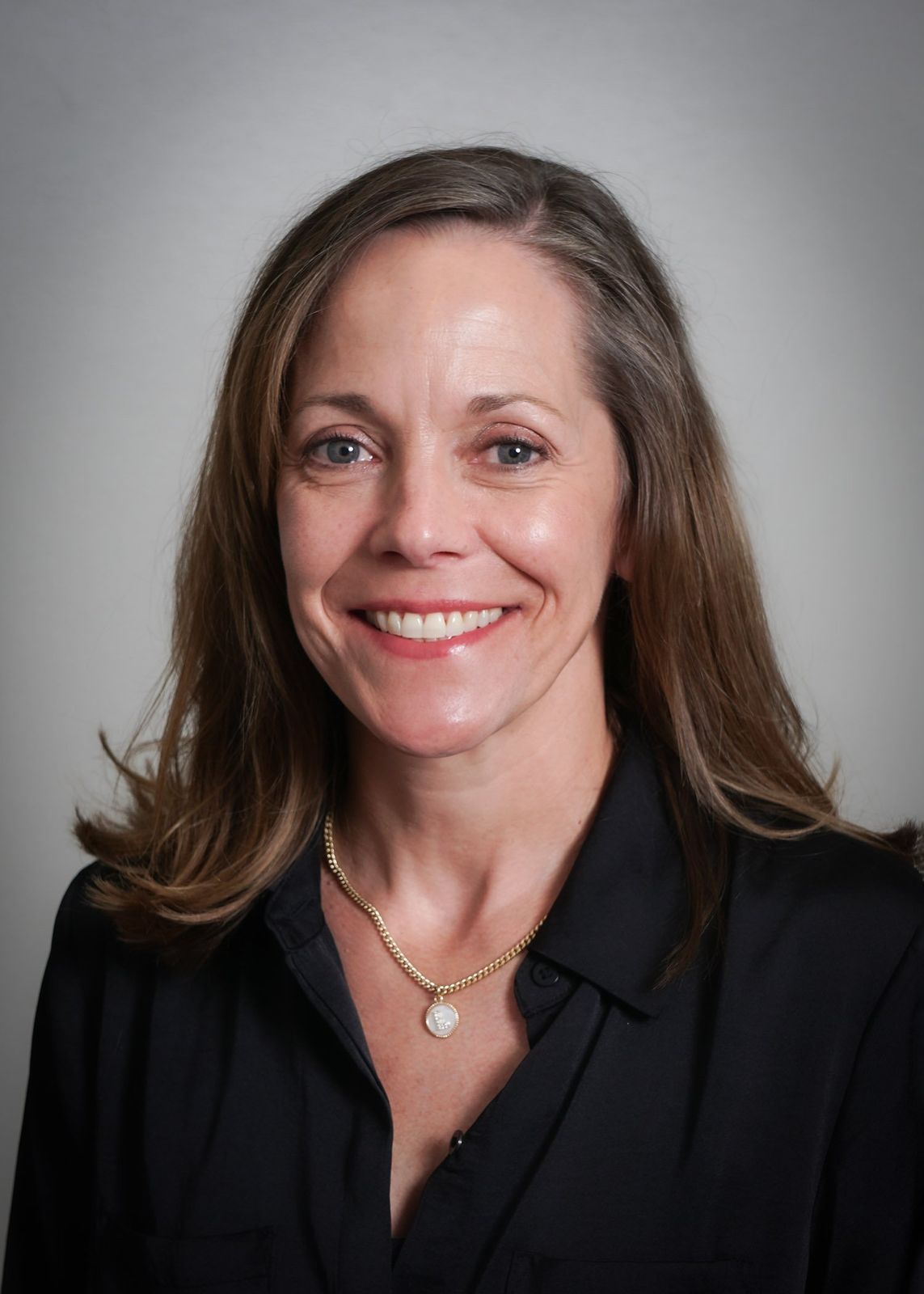 A woman wearing a black shirt and a necklace is smiling for the camera.