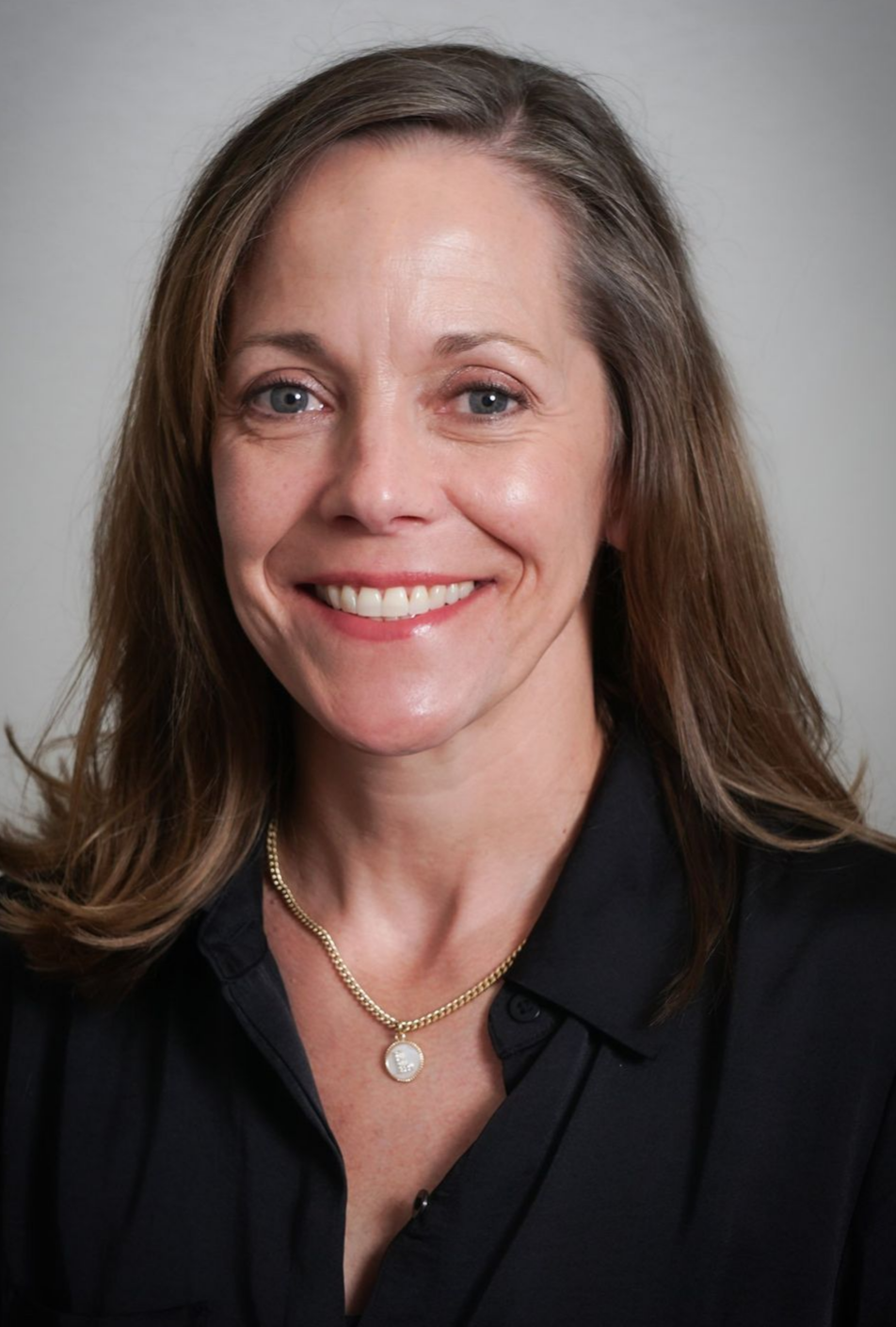 A woman wearing a black shirt and a necklace is smiling for the camera.