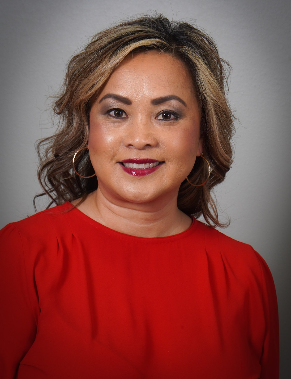 A woman wearing a red shirt and earrings is smiling for the camera.