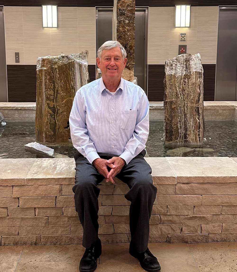 A man is sitting on a stone wall in front of a fountain