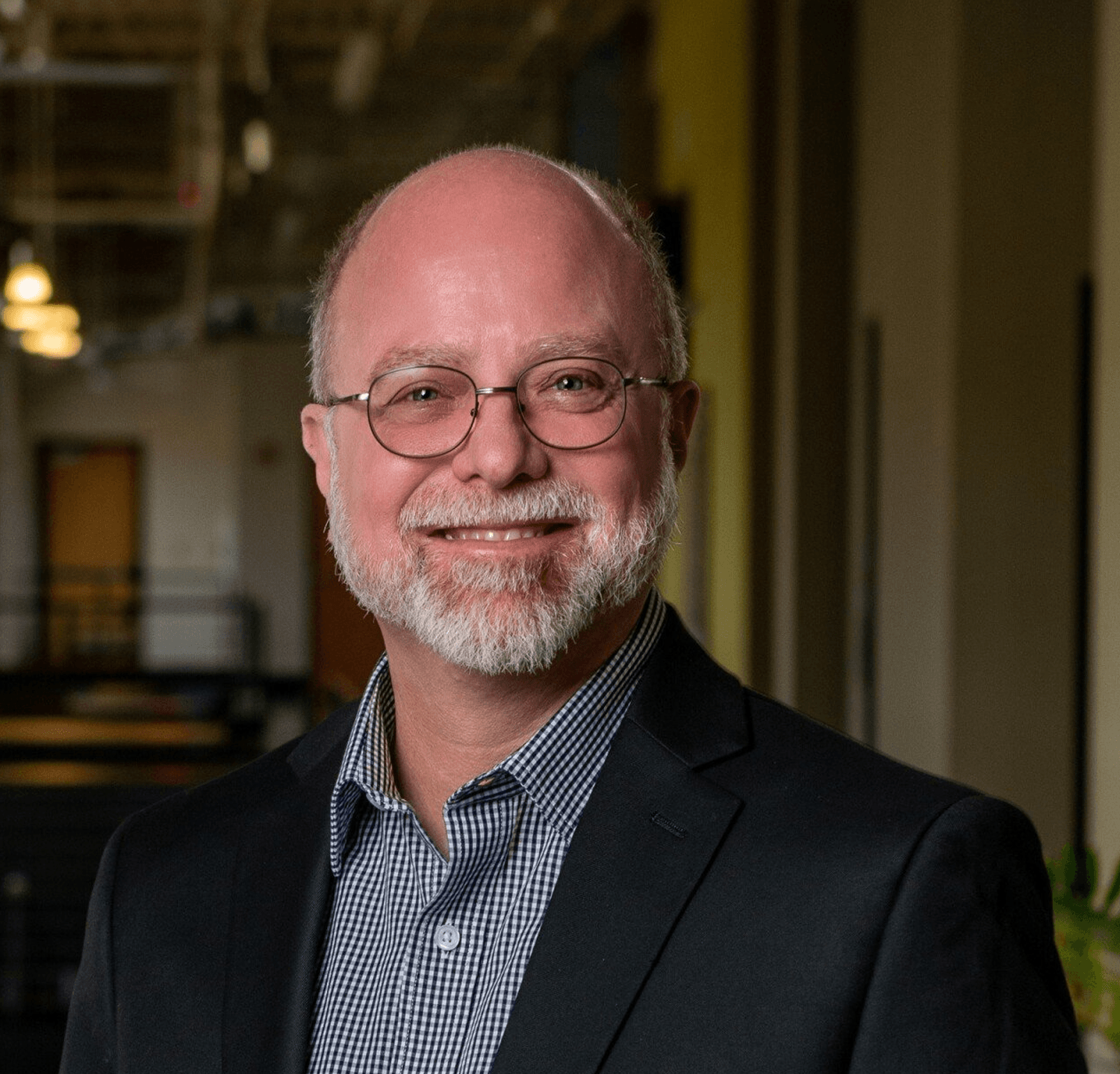 A bald man with a beard and glasses is wearing a suit and smiling.