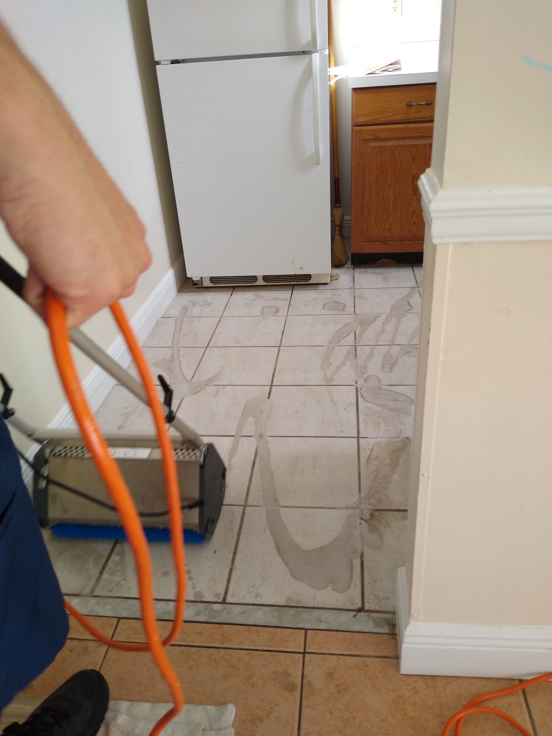 A person is cleaning a tiled floor with an orange cord
