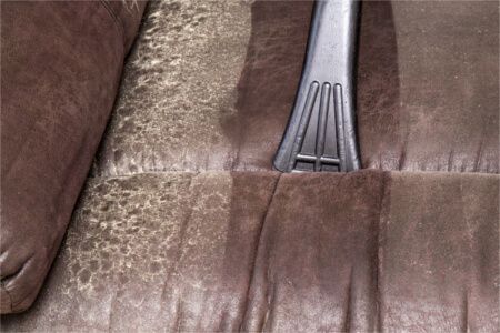 A vacuum cleaner is cleaning a brown couch.