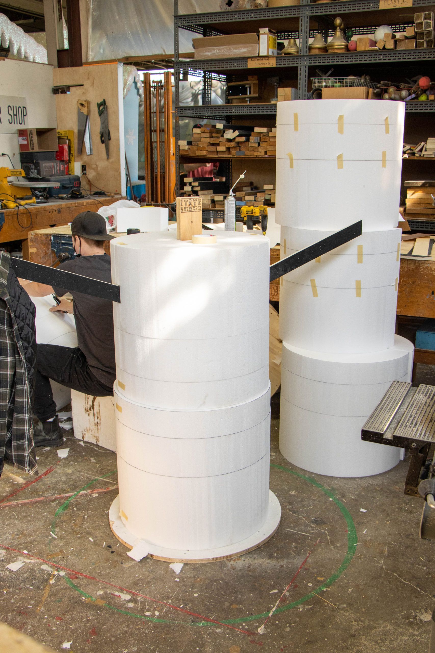 A man is working on a stack of styrofoam cylinders in a workshop.