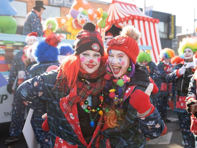 Two women dressed as clowns are posing for a picture in a parade.