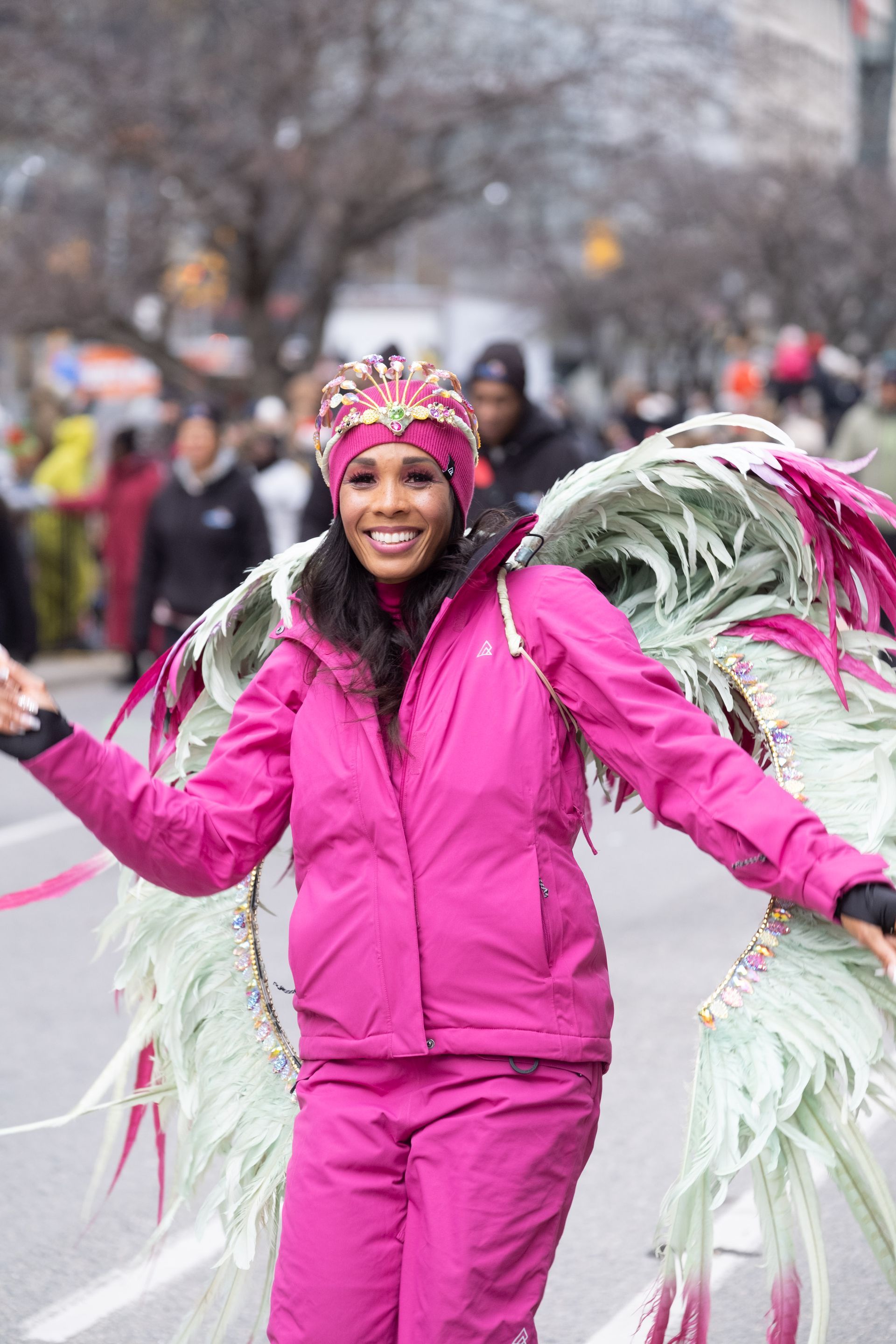 A woman in a pink jacket and pants is wearing wings and a hat.