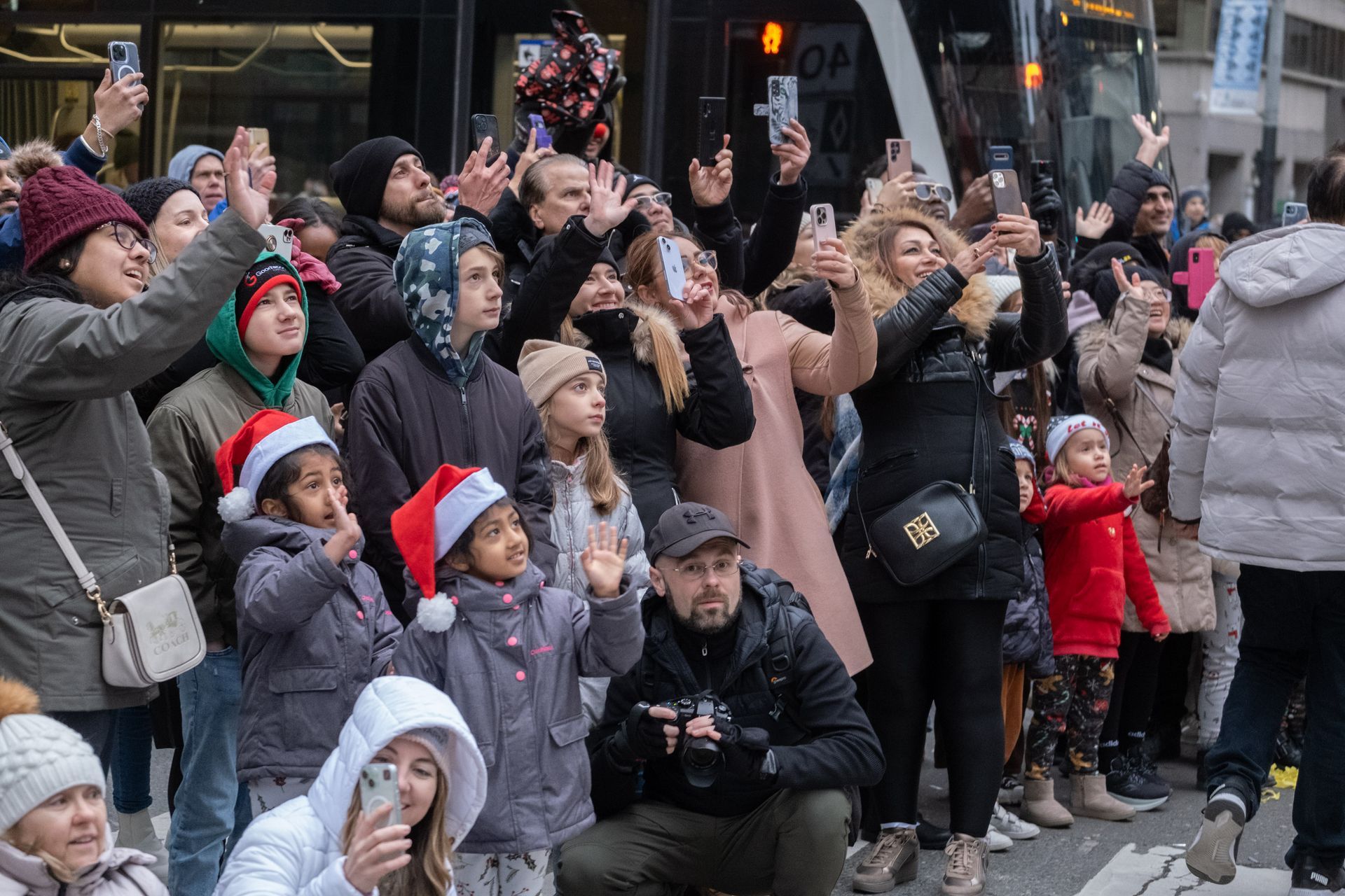 A group of people are taking pictures of a parade with their phones.