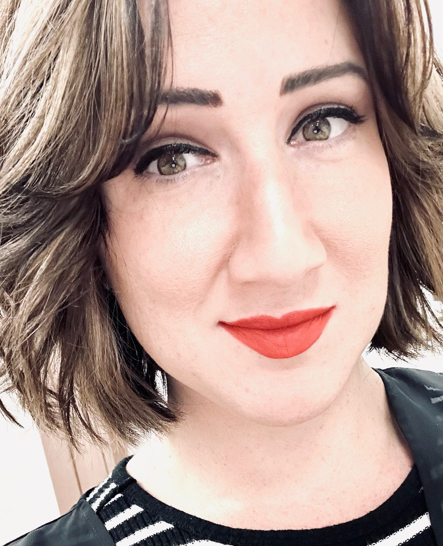 Woman with brown hair, red lipstick, and black/white striped shirt smiles.