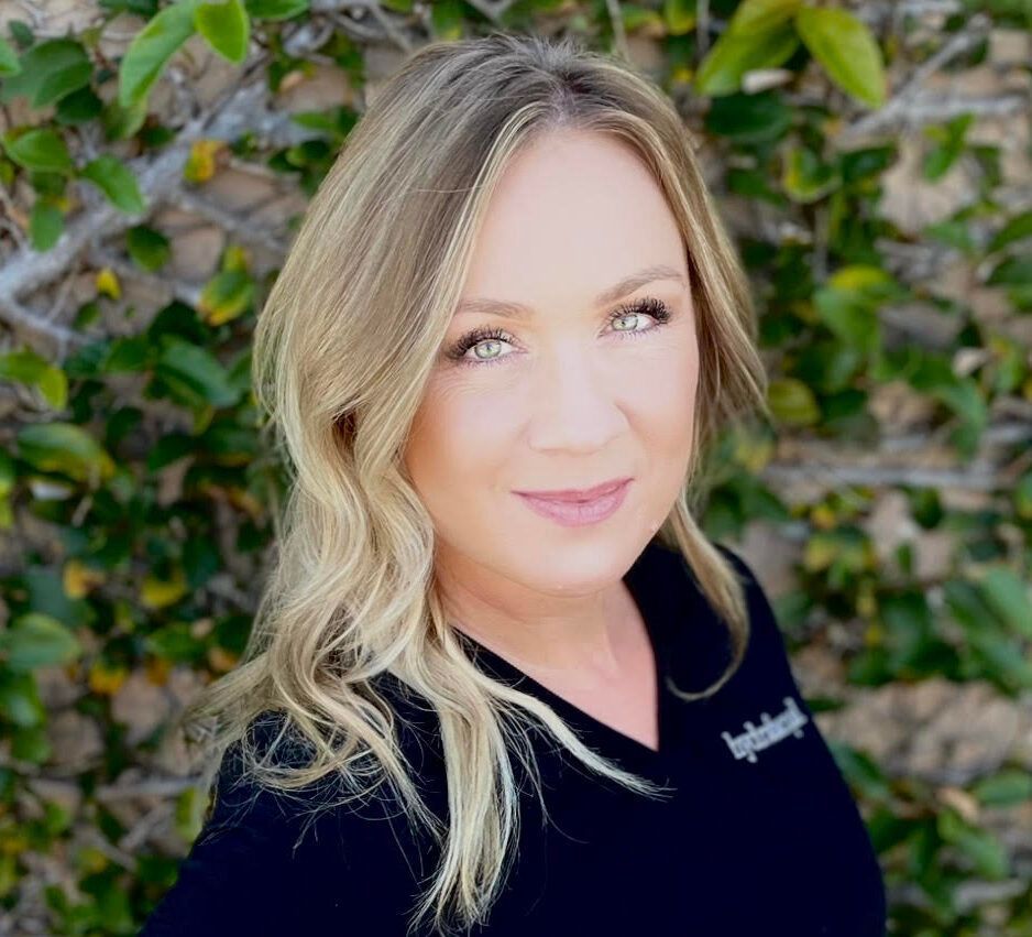 Woman with blonde hair smiles in front of a green wall, wearing a black shirt.