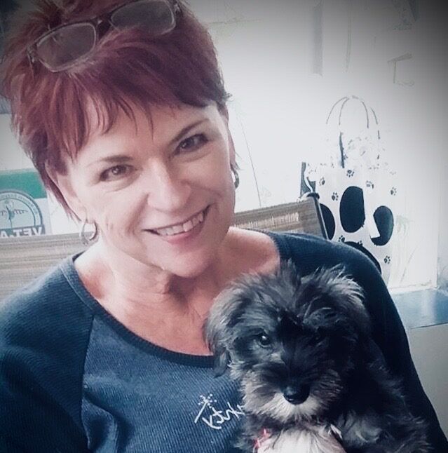 Woman with red hair smiles while holding a small black and gray puppy.